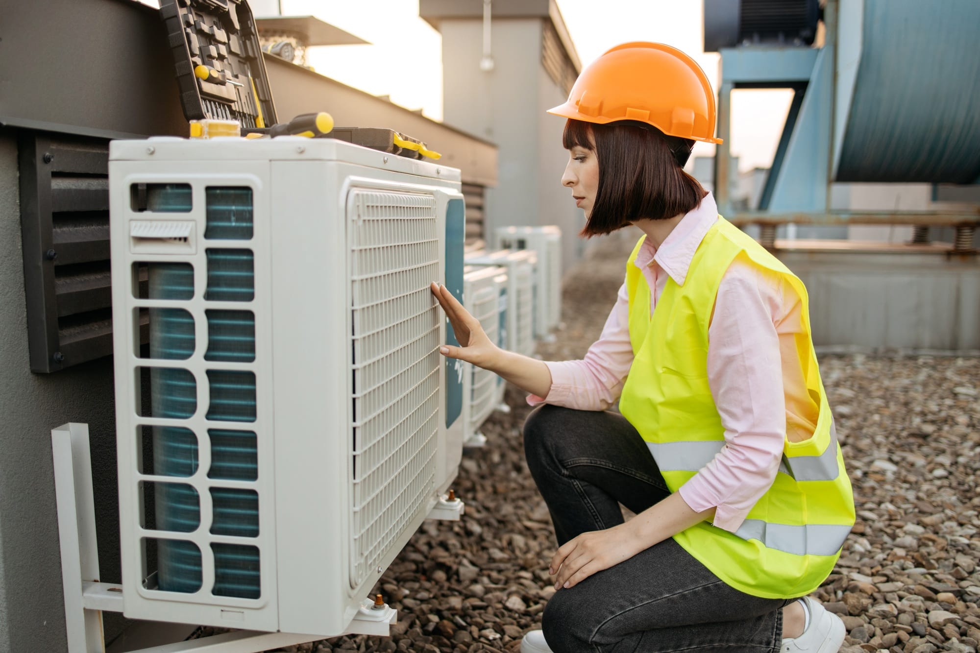 Female employee kneeling near air conditioner outdoors